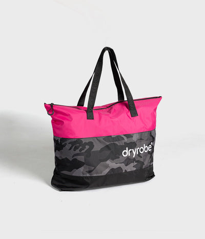 A Dryrobe tote bag with a bright pink top half, a black and gray camouflage lower half, and black shoulder straps, shown on a light gray background.