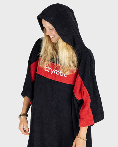 Woman wearing Organic Towel dryrobe Remix in Black Red with hood up looking down to the left