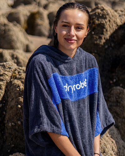 Woman with wet hair sitting on rocks, wearing Organic Towel dryrobe Remix in Navy Royal Blue
