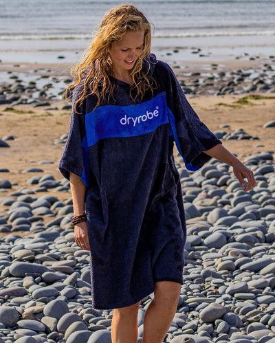 Woman walking over pebbles on a beach, wearing Organic Towel dryrobe Remix in Navy Royal Blue