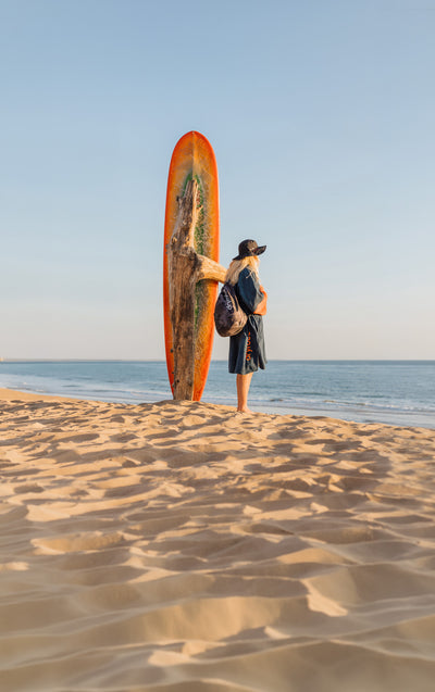 Person holding a surfboard on a sandy beach with ocean and clear sky in the background