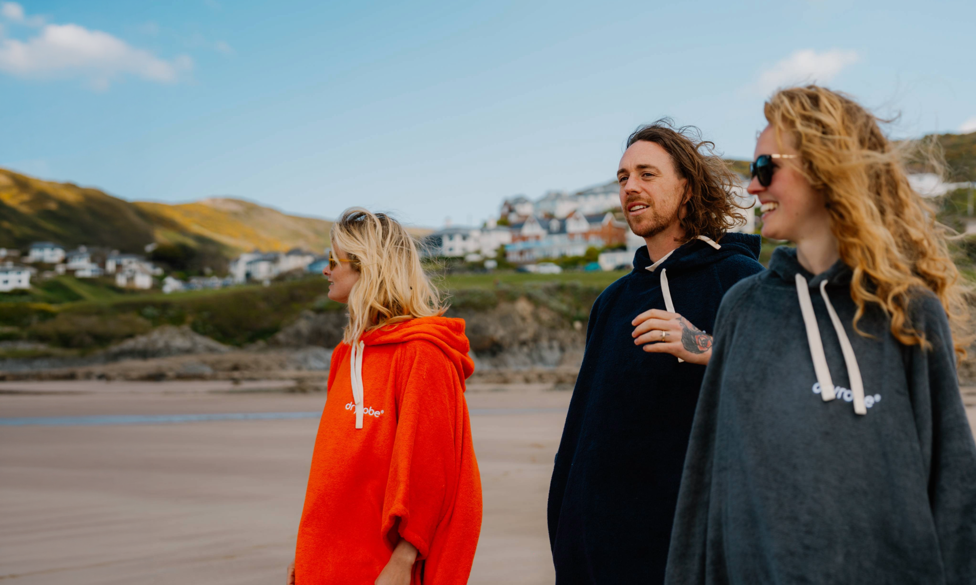 Three people wearing towel robes on a beach with a scenic background