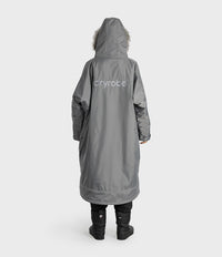 A person shown from the back wearing a long gray hooded dryrobe with a white 'dryrobe' logo on the back, black pants, and black boots against a light gray studio background.