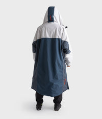 A person shown from the back wearing a hooded Dryrobe in white and navy blue, standing against a light grey studio background.