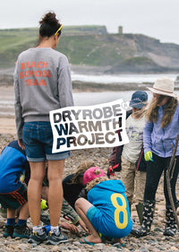 An adult and group of children picking litter off a beach, featuring dryrobe® warmth project logo 