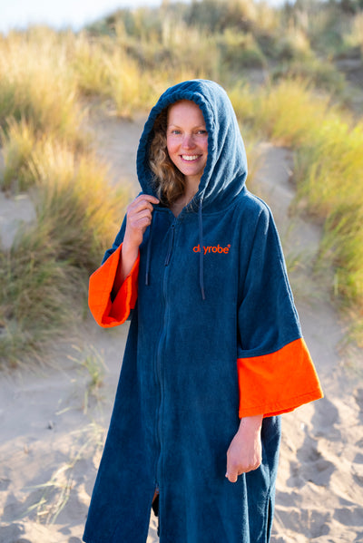 Person wearing a blue and orange hooded towel robe on a sandy path with grasses.