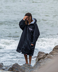 Man stood on rocks on a beach, wearing Black Grey Camo dryrobe Advance Long Sleeve REMIX Range