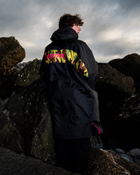 Man stood on a beach, wearing Black Pink Camo dryrobe Advance Long Sleeve REMIX Range