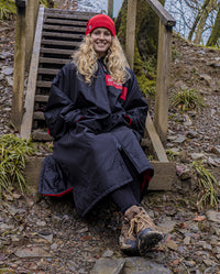 Woman sat on wooden steps, wearing Black Red Red dryrobe® Advance Long Sleeve REMIX Range 