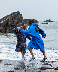 Two people running on a beach by the sea, wearing dryrobe® Advance Long Sleeve REMIX Range