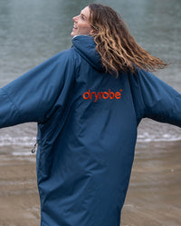 Girl stood smiling on a beach with back to the camera, wearing Limited Edition RNLI dryrobe Advance