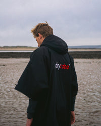 Man walking on a beach with back to the camera, wearing Black Grey dryrobe® Advance Short Sleeve