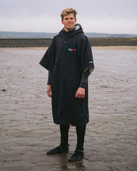 Man stood on beach in wetsuit and Black Grey dryrobe® Advance Short Sleeve