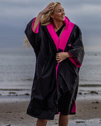 Woman stood in front of the sea, wearing Black Pink dryrobe® Advance Short Sleeve unzipped