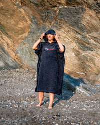 Woman stood on a beach wearing Navy Blue Organic Towel dryrobe® with hood up