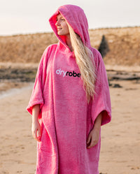 Woman stood on a beach wearing Pink Organic Towel dryrobe® with hood up