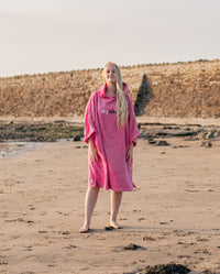 Woman stood in the sun on a beach, wearing Pink Organic Towel dryrobe®