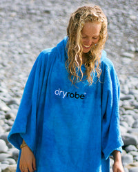 Woman with wet hair smiling on a beach, wearing  Cobalt Blue Organic Towel dryrobe®