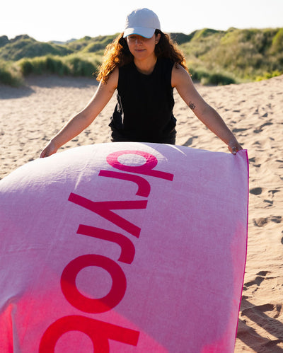 Woman on beach laying out pink Dryrobe® beach towel on the sand 