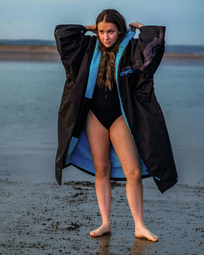 Adult female on beach wearing black blue remix Dryrobe®