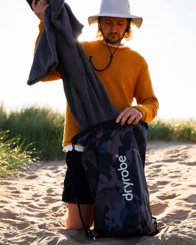 Male on beach unpacking black camo Dryrobe® compression bag 
