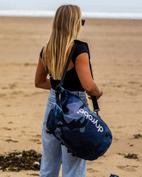 Woman stood on beach holding dryrobe Compression Travel Bag in Blue Camo on shoulder