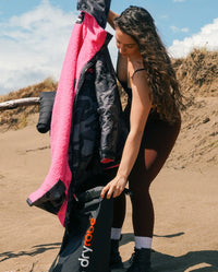 Woman putting dryrobe® Advance into dryrobe® Compression Travel Bag while stood on the beach