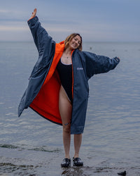 Woman on beach wearing grey orange Dryrobe® LS Advance