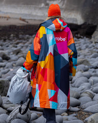 Woman walking along rocky beach, wearing dryrobe Advance Abstract and Beanie