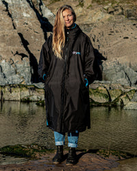 Woman stood on beach in front of rocks, wearing Black Blue dryrobe® Advance Long Sleeve