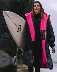 dryrobe® ambassador Lucy Campbell holding surfboard, wearing Black Camo Pink dryrobe® Advance Long Sleeve
