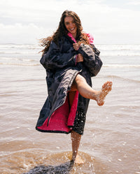 Woman stood in sea kicking water, wearing Black Camo Pink dryrobe® Advance Long Sleeve