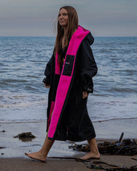 Woman walking on a beach, wearing Black Pink dryrobe® Advance Long Sleeve
