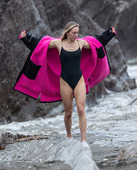 Woman stood by the sea, putting on Black Pink dryrobe® Advance Long Sleeve