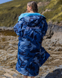 Woman on a beach with back to the camera, wearing dryrobe Advance Long Sleeve changing robe in Blue Camo Blue