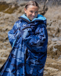 Woman on a beach wearing dryrobe Advance Long Sleeve changing robe in Blue Camo Blue, wrapping it around herself 