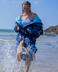 Woman on a beach splashing through shoreline, wearing swimsuit underneath dryrobe Advance Long Sleeve changing robe in Blue Camo Blue