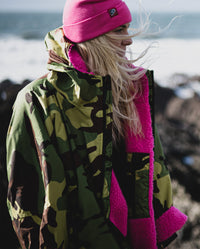 Woman stood on a beach wearing Camo Pink dryrobe® Advance Long Sleeve and Pink dryrobe® Eco Beanie