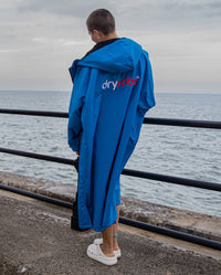Woman stood by the sea with back to the camera, wearing Cobalt Blue Black dryrobe® Advance Long Sleeve