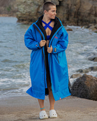 Woman walking on a beach in swimsuit, wearing Cobalt Blue Black dryrobe® Advance Long Sleeve
