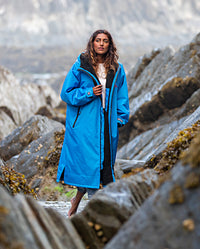 Woman walking through rocks on a a beach, wearing Cobalt Blue Black dryrobe® Advance Long Sleeve