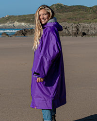 Woman stood smiling on a beach, wearing Purple Grey dryrobe® Advance Long Sleeve 