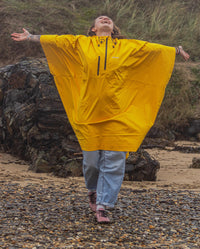 Woman walking towards camera on a beach with arms out to the side, wearing  Yellow dryrobe® Waterproof Poncho