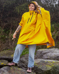 Woman stood on a rock smiling, wearing  Yellow dryrobe® Waterproof Poncho with hood up 