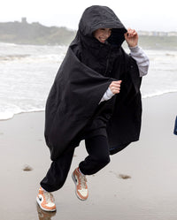 Girl running in the rain on a beach, smiling, wearing Black Kids dryrobe® Waterproof Poncho