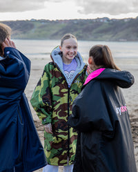 Three girls stood on beach talking, wearing dryrobe® Advance Kids Long Sleeve