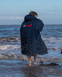 Boy stood in sea facing away from camera wearing Navy Grey dryrobe® Advance Kids Long Sleeve