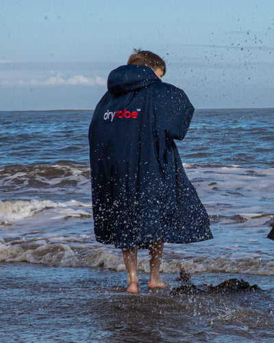 Boy stood in sea facing away from camera wearing Navy Grey dryrobe® Advance Kids Long Sleeve