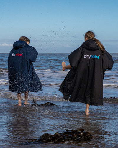 Two kids splashing in the shoreline, wearing dryrobe® Advance Kids Long Sleeve