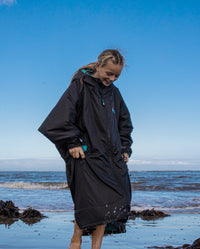 Girl stood on beach in front of the sea, wearing Black Blue dryrobe® Advance Kids Long Sleeve